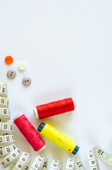 Sewing accessories. Flat lay of spools of colored thread, pin, centimeter and buttons on white background. Copy space