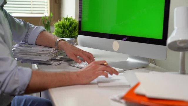 Motivated businessman making accounts on desktop computer in office. Young expert writing down new idead, analyzing graphics and diagrams and calculating figures. Paperwork in office. Investment and