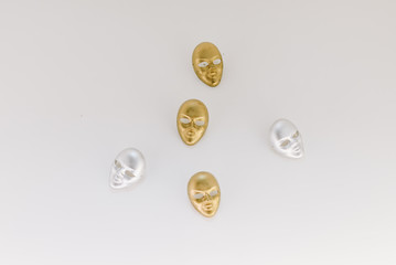 Five small golden and silver masks top-down lay flat on a white background