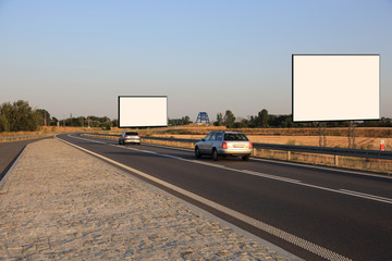 Fototapeta Puste bilbordy reklamowe przy drodze szybkiego ruchu o zachodzie słońca, samochody osobowe. obraz