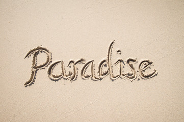 Paradise message handwritten on the smooth sand of an empty beach with copy space