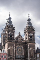 Fototapeta premium Red brick with white trim upper part facade Basilica of Saint Nicolas under gray cloudscape showing towers and statues.