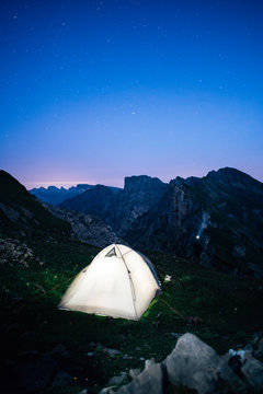 person with a head lamp next to an illuminated tent on a mountain ridge 