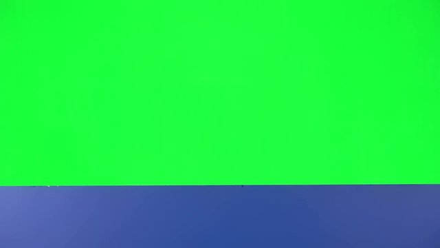 Girl looking out from behind blue blank placard on green screen at studio. The board is horizontal