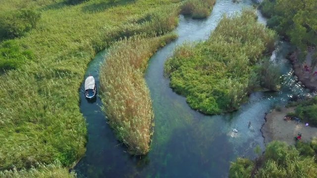 Aerial top view of Akyaka river and reeds - People swimming - A boat trips on the river and drone flying down