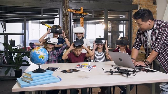 Group of six cheerful young caucasian students wearing VR headset working together with male korean teacher on a Programing Project during a class - Powered by Adobe