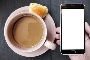 view from above flat lays hand holding smartphone with brown cup of coffee and bread on black wooden table