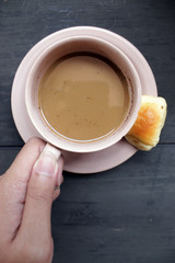view from above flat lays hand holding brown cup of coffee and bread on black wooden table