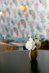 Restaurant table with white flowers in gold round vase, party decor, minimal wedding reception decor