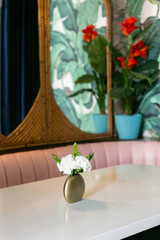 White flowers in gold vase on table at restaurant booth, pink couch, rattan mirrors and flower wallpaper