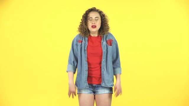 Girl carefully examines something then fearfully covers her face with her hand on yellow background at studio.