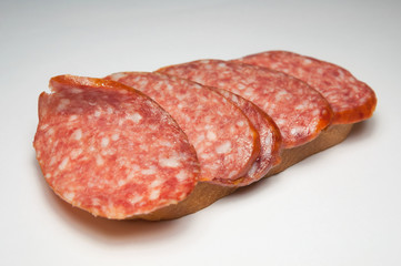 Red salami sandwich. Slices of red salami sausage and a loaf. Product for a snack at work. Sliced sausage hanging from a loaf.