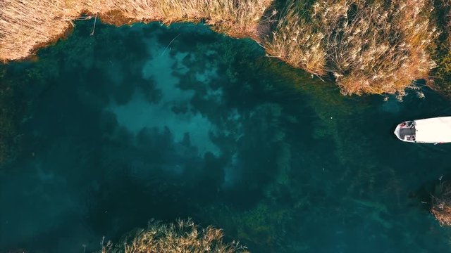 Aerial top view of Akyaka river and reeds - Bottom of the river is visible and see river weeds and turquise color - Two river boats going to opposite