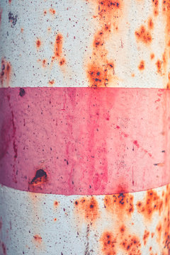 Rusty metal road post painted in pink and white horizontal stripes. Street sign