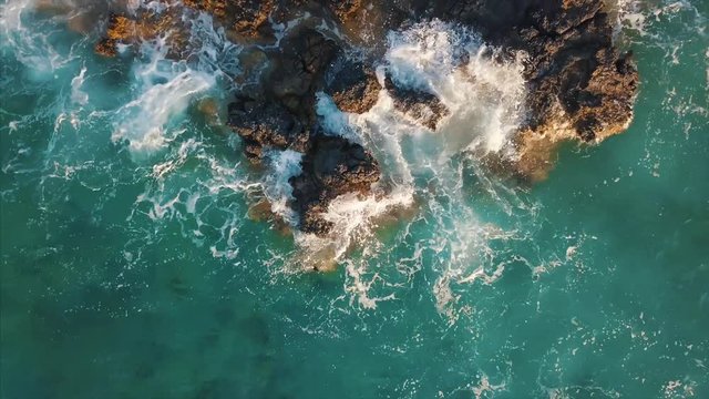 Aerial top view of sea wave hitting cliffs of a rocky coast  - drone moves up and high
