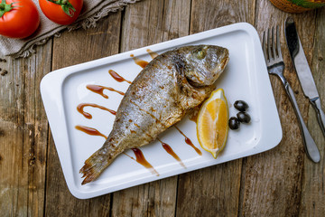 Dorado on grill on white plate on wooden table