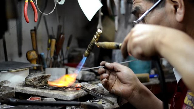 Master jeweler welding an ornament in a jewelry workshop. Image of hands and product close up.