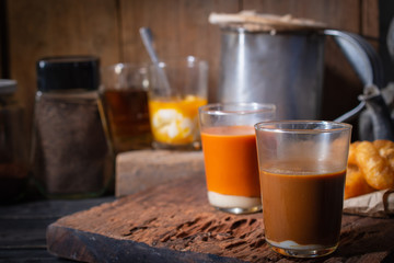 Traditional Thai hot coffee with milk on the wood table there are Traditional Thai hot tea, deep-fried doughstick (patongko), hot tea and soft-boiled egg plated around.