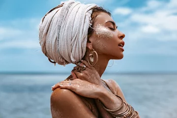 Schließen Sie herauf Porträt der schönen jungen Stammes- Frau im Turban am blauen Meer- und Himmelshintergrund © zolotareva_elina