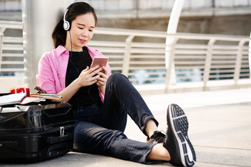 Asian female traveler is sitting for tourist information on a smartphone. During the summer holidays, there are amazing places like resorts, shopping centers or street food. copy space