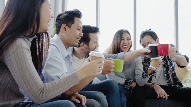 Diversity of young people group team holding coffee cups and discussing something with smile while sitting on the couch at office. Coffee break time at creative office.