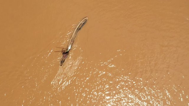 Bird's eye aerial perspective of local farmer paddling in traditional dugout boat (canoe) on Omo river in Ethiopia, manual labor and poverty in Africa