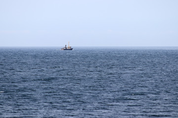 Fishing boat on horizon departing to the sea.