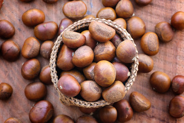 Ripe chestnuts in wicker basket on wooden background