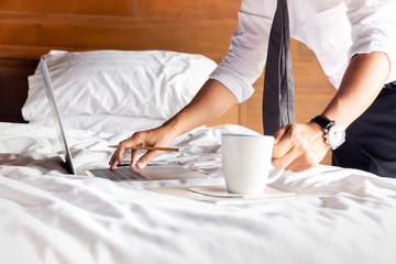 Businessman working on laptop with hand holding coffee mug in bedroom.