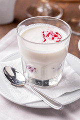 glass of milkshake with berry syrup close-up, white saucer, teaspoon  and linen napkin on table 