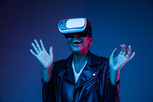 Portrait of young african-american woman's playing in VR-glasses in neon light on blue background. Concept of human emotions, facial expression, modern gadgets and technologies. Look astonished, happy
