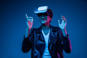 Portrait of young african-american woman's playing in VR-glasses in neon light on blue background....