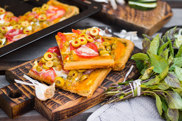 Homemade vegan pizza baked on tray. Square Italian vegetarian pizza pieces with olives, tomatoes. 