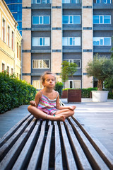 LIttle girl sit in lotus position asana. Kid make yoga in the modern city.