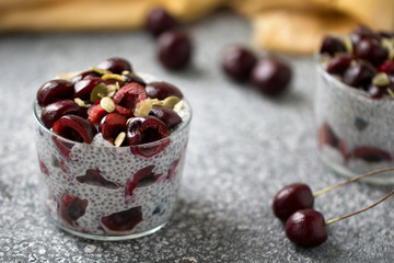 Chia pudding with cherry berries, natural yogurt, chia, pumpkin seeds in a glass on a grey surface. Front view. Healthy dessert,  super food 
