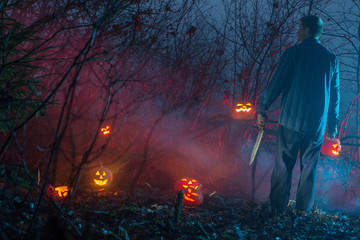 scary man in night  forest is cutting Halloween pumpkins