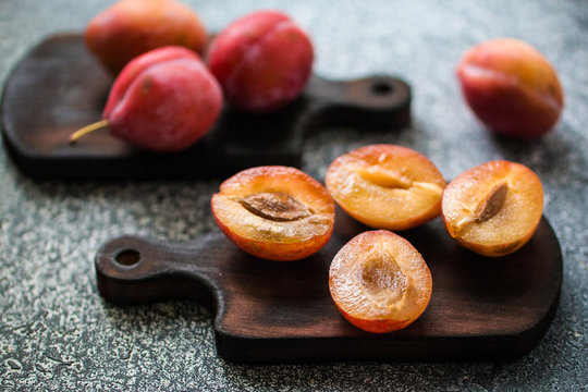 Whole and cut ripe plums on a wooden board on a grey table. Preparation of the pie. Front view