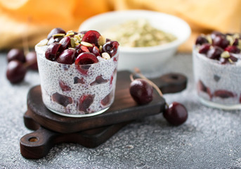 Chia pudding with cherry berries, natural yogurt, chia, pumpkin seeds in a glass on a grey surface. Front view. Healthy dessert,  super food 