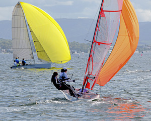 Children Sailing small sailboats with yellow and orange sails on an inland waterway.