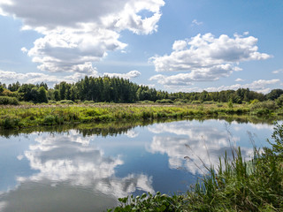 river in countryside in summer. cloudy sky reflected on water surface