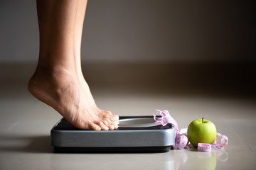 Fototapeta premium Female leg stepping on weigh scales with measuring tape and green apple. Healthy lifestyle, food and sport concept.