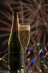 Vertical image of an elegant green bottle of champagne behind a glass with yellow champagne and many blurred Christmas lights in the background. Concept of Christmas celebration.