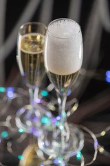 Aerial view of a luxurious and sparkling champagne served in a glass next to another glass with champagne and in the background many unfocused artificial lights. Concept of celebration.