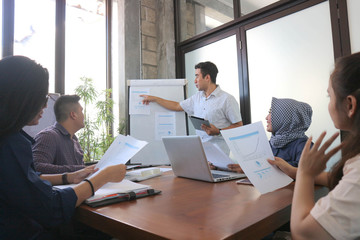 young professional male presentation at group meeting in white board with tablet and laptop, office meeting group