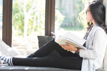 beautiful Asian women with glasses reading books while shiting by the window comfortably on a sunny...