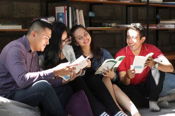 group of happy asian friends reading books and laughing at library on a sunny day