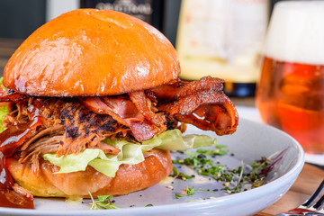 A Pulled Pork Burger with bacon, lettuce and barbecue sauce in a bead bun