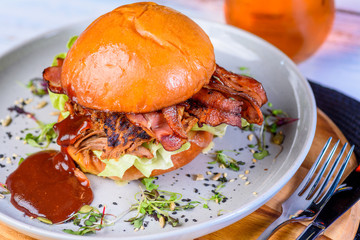 A Pulled Pork Burger with bacon, lettuce and barbecue sauce in a bead bun