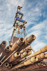 In the foreground are drill pipes. In the background is a blurred image of a drilling rig for...