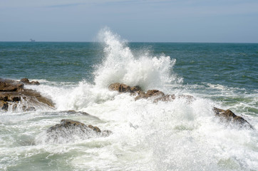 Wave with foam breaking of rock in ocean or sea